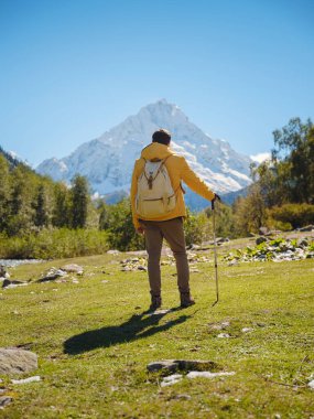 Irkis Vadisi 'nden, Arkhyz' den, Karachay-Cherkessia 'dan, Kuzey Kafkasya' dan. Mavi gökyüzü, bulutlar ve Kafkasya nehri yakınlarındaki güzel ormanla karlı dağ vadisinde yürüyüş yapan bir adam..