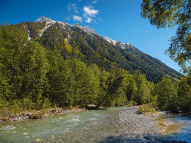Irkis Vadisi 'nden, Arkhyz' den, Karachay-Cherkessia 'dan, Kuzey Kafkasya' dan. Mavi gökyüzü ve bulutlarıyla karlı dağ vadisi ve Kafkasya 'da Psysh nehrinin yakınında güzel bir orman. Alp manzarası.