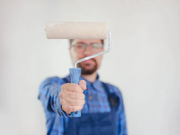 young man in blue work suit hold paint roller, isolated on white wall background. Instruments accessories for renovation apartment room. Repair home concept