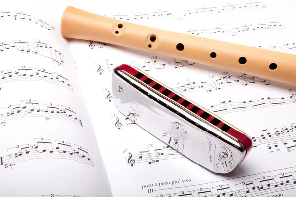 Mouth harmonica and wooden flute on sheet music. Close up. — Stock Photo, Image