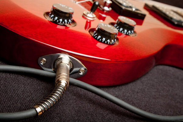 Detail of a wine red color electric guitar with cord plugged into the jack.