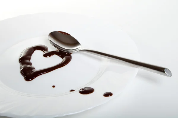 Melted dark chocolate on plate and steel spoon. Heart shape — Stock Photo, Image