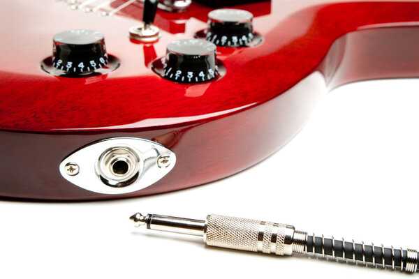 Detail of a wine red color electric guitar with cord.