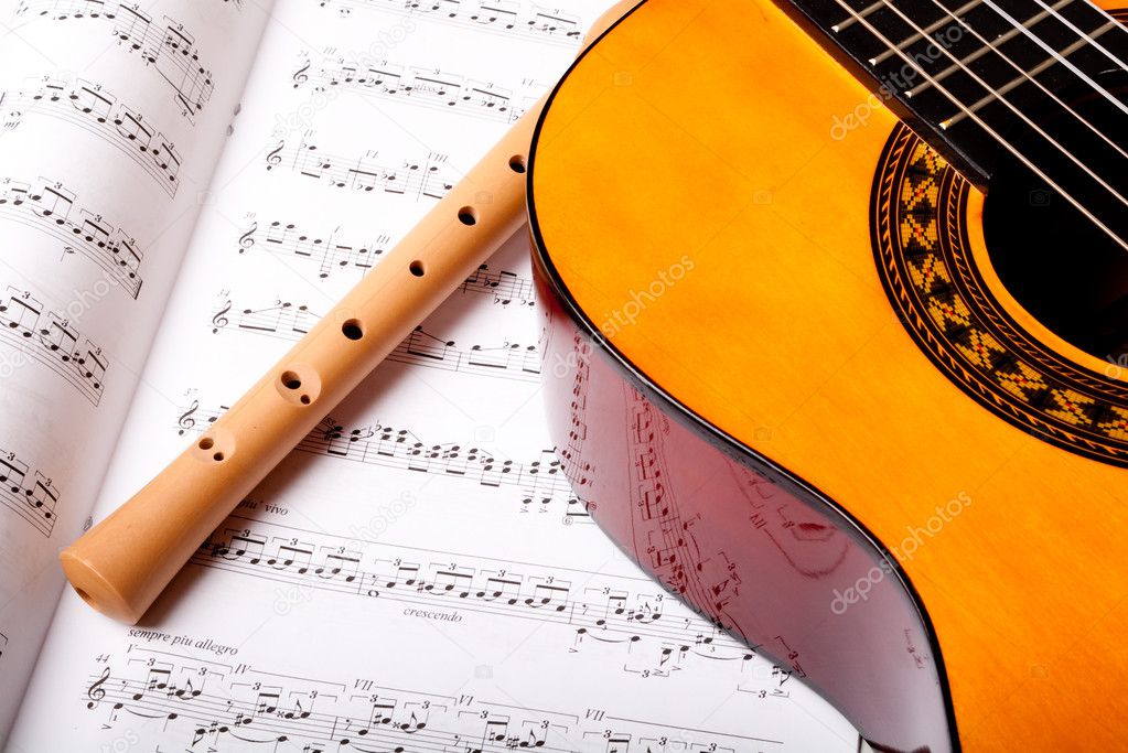 Wooden flute and classic acoustic guitar on sheet music. Close up.