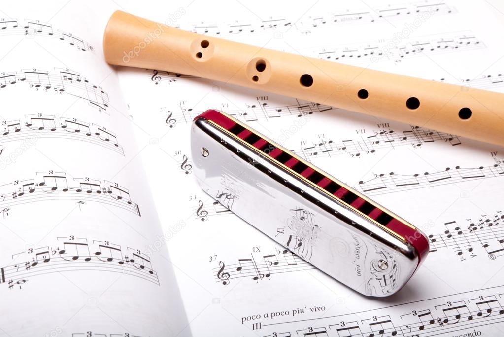 Mouth harmonica and wooden flute on sheet music. Close up.