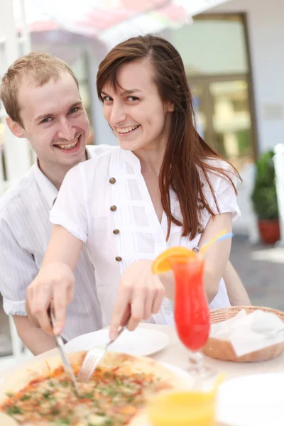 Young couple cutting pizza in cafe — Stock Photo, Image