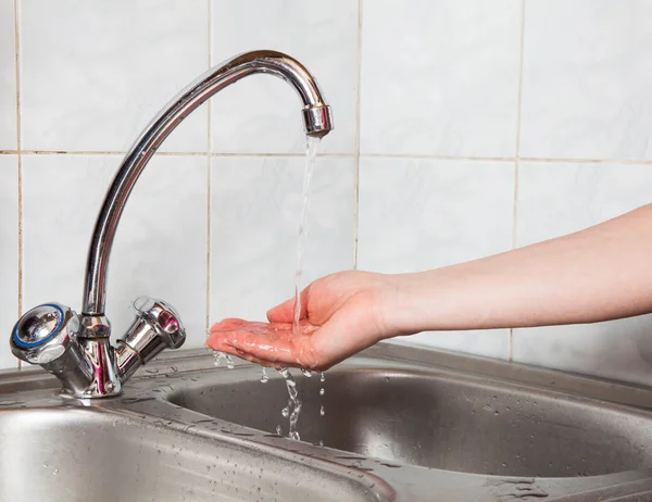 Una mano femenina bajo el agua corriente en el fregadero — Foto de Stock