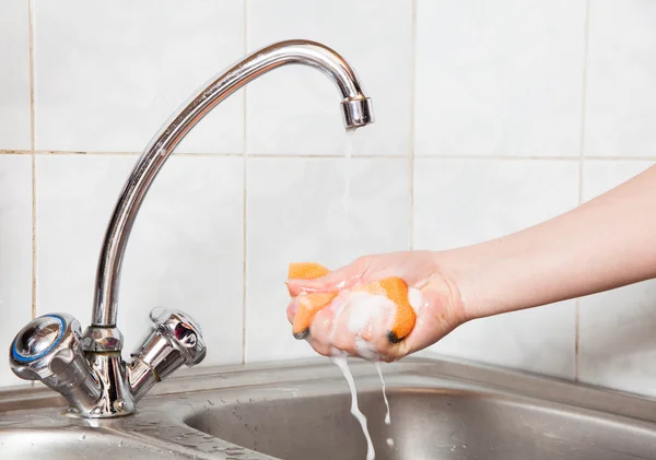 Female hands holding a sponge in soap under the running water — Stock Photo, Image