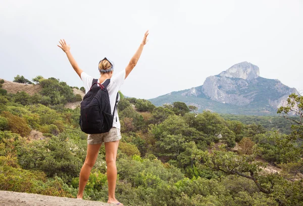 Young happy woman with backpack relaxing on a rock — Stock Photo, Image