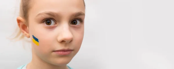 Face of a frightened girl, a painted heart on the cheek in yellow-blue colors of the Ukrainian flag. — Stock Photo, Image