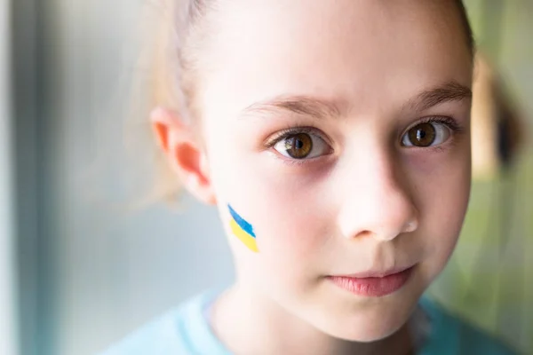 Ansikte av en rädd flicka, ett målat hjärta på kinden i gul-blå färger på den ukrainska flaggan. — Stockfoto