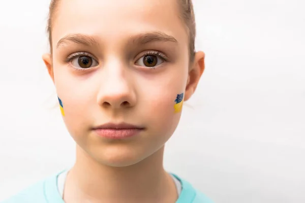 Ansikte av en rädd flicka, ett målat hjärta på kinden i gul-blå färger på den ukrainska flaggan. — Stockfoto