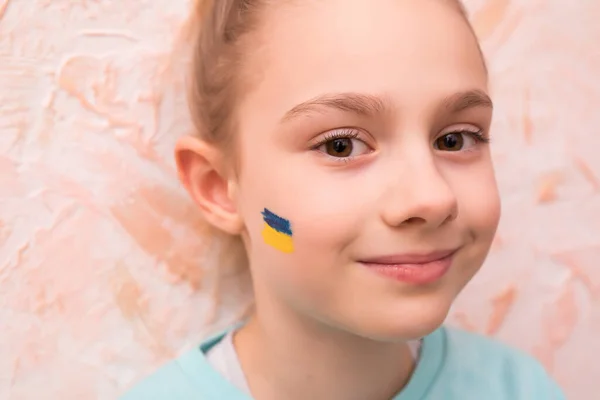 Rostro de una niña asustada, un corazón pintado en la mejilla en colores amarillo-azul de la bandera de Ucrania. — Foto de Stock