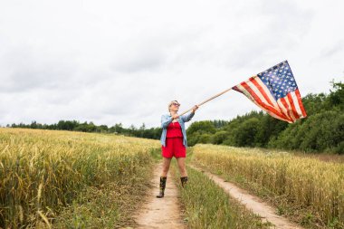 Young smiling girl on the field waving with the USA flag