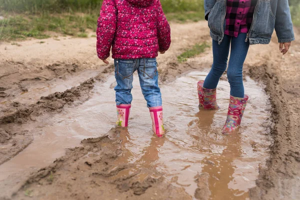Two smiling girls run through the puddles and play.