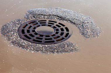 Melted water flows down through the manhole cover on spring day clipart