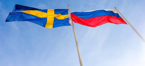 Flags of Russia and Sweden waving against blue sky — Stock Photo, Image