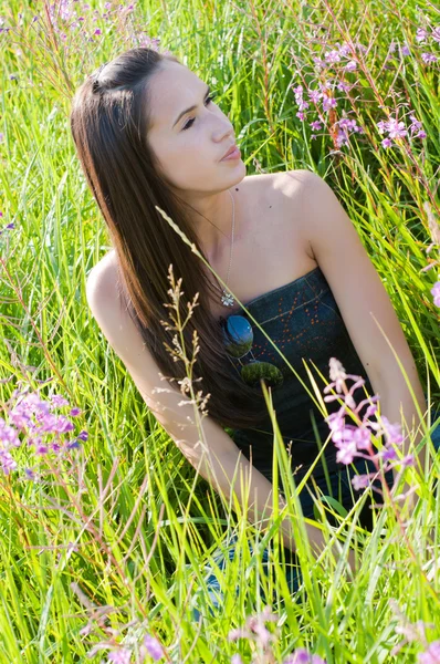 Beautiful brunette woman sitting in field — Stock Photo, Image