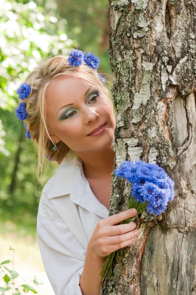 Женщина с голубыми цветами подглядывает из-за дерева — стоковое фото