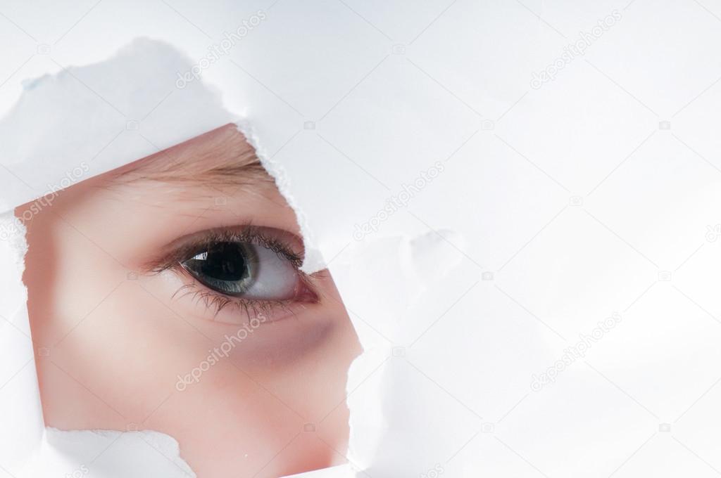 Child eye looking through a hole in paper