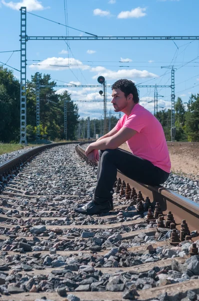 Een man in roze t-shirt zittend op treinrails — Stockfoto