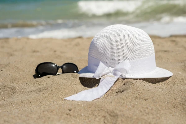 Chapéu branco de vime e óculos de sol na praia — Fotografia de Stock