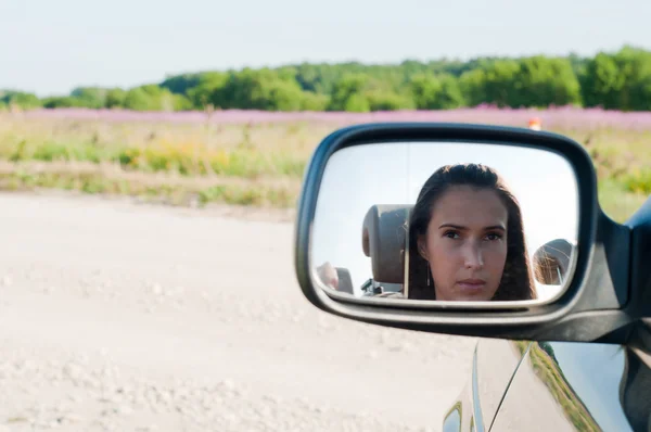 Mujer joven cara en el espejo del coche — Foto de Stock
