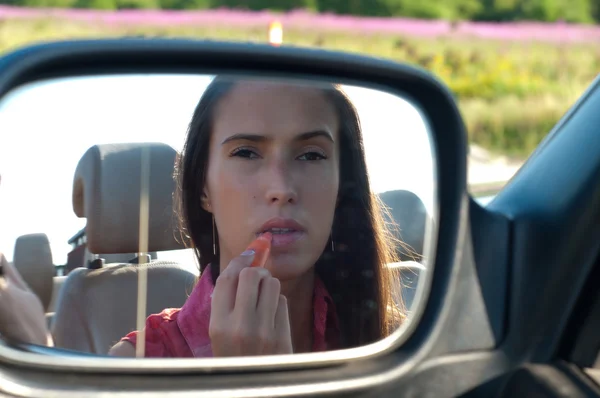 Mujer aplicando lápiz labial mirando el espejo del coche — Foto de Stock