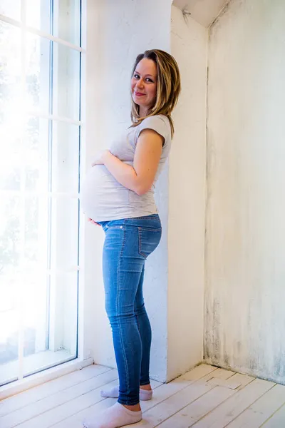 Schöne schwangere Frau steht zu Hause am Fenster — Stockfoto