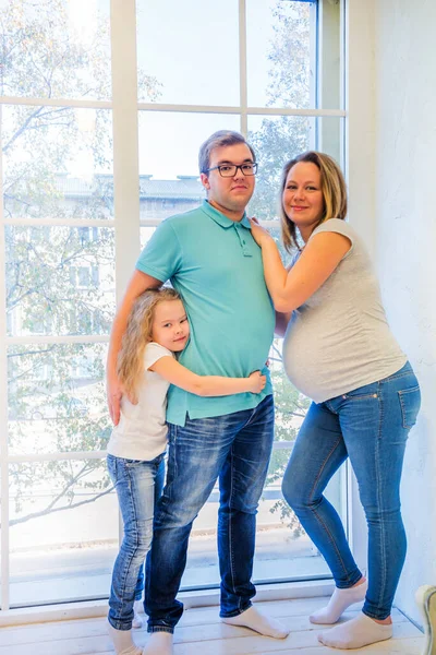 Schöne schwangere Frau, Mädchen und Mann am Fenster — Stockfoto