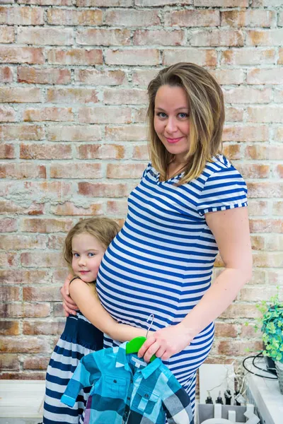 Beautiful pregnant woman with daughter near the wall — Stock Photo, Image