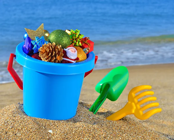 Christmas decorations in a baby bucket and toys on the beach — Stock Photo, Image