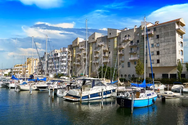 Beautiful view of the pier with boats, yachts and a high-rise building on the shores of the picturesque Mediterranean canal in the Golf de Roses against the blue sky in the city. Empuriabrava, Spain.