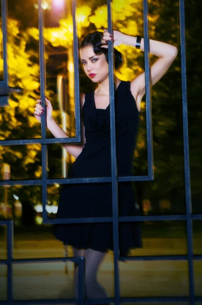Pretty woman posing in cage outdoors at night — Stock Photo, Image