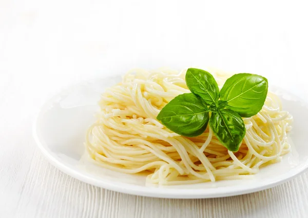 Паста-спагетти и зеленый лист базилика на белой тарелке — стоковое фото