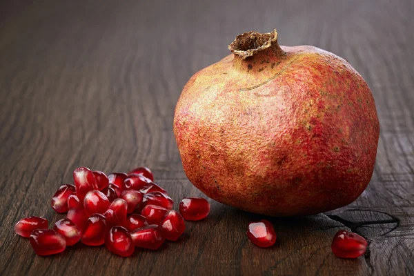Pomegranate and seeds on wooden table — Stock Photo, Image