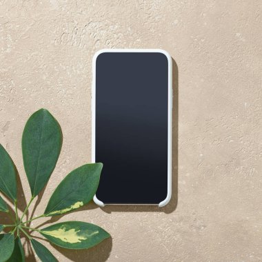 akıllı telefon ve yeşil yaprak bej renkli masa, üst görünüm