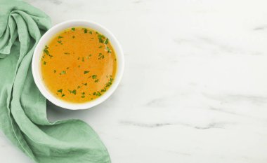 bowl of fresh chicken broth on light kitchen table, top view