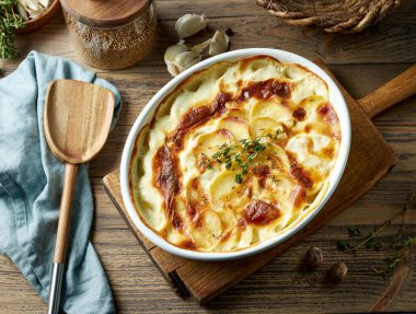 Kırsal ahşap mutfak masasında taze pişmiş patates graten tabağı.