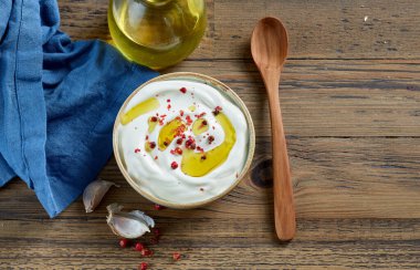 bowl of sour cream or greek yogurt decorated with olive oil and red pepper on wooden kitchen table, top view