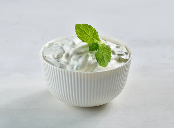 bowl of sour cream or greek yogurt tzatziki sauce decorated with mint leaf on white kitchen table