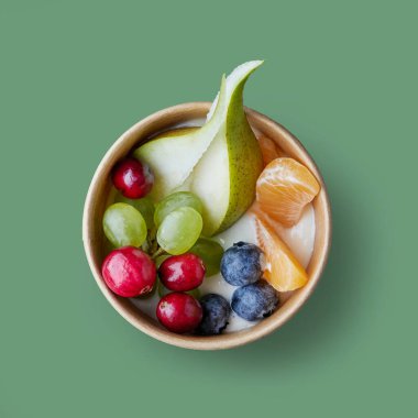fresh fruit, berries and yogurt in paper cup isolated on green background, top view