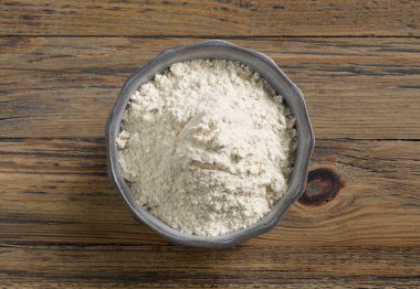 Ahşap mutfak masasında bir kase un, üst manzara.