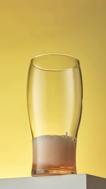 在黄色背景下倒入玻璃杯的啤酒的垂直格式化停止运动动画 — 图库视频影像