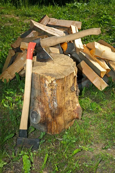 Machado que divide o martelo e corta a madeira de fogo em uma grama verde — Fotografia de Stock