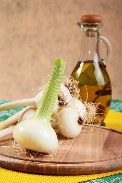 Cebolla y ajo con una botella de aceite de oliva en una mesa de cocina —  Fotos de Stock