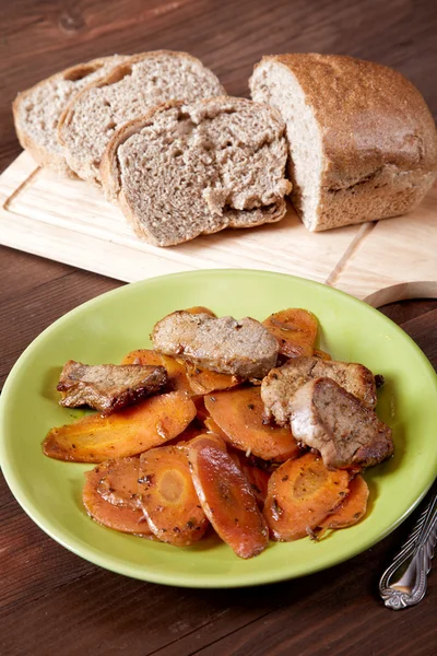 El plato con la carne y la zanahoria el pan cortado sobre la mesa de la cocina —  Fotos de Stock