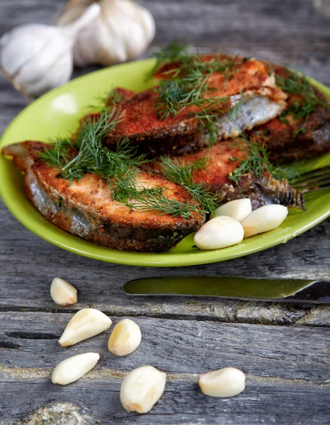 Kızarmış balık ve ahşap bir masa üzerine sarımsak ile plaka — Stok fotoğraf