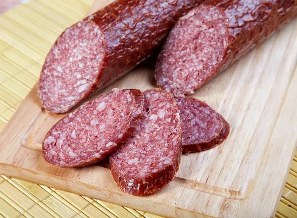 La saucisse fumée coupée sur une planche de bois — Photo