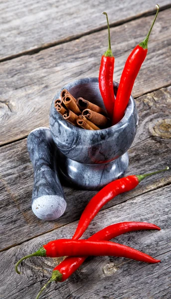 Mortar with cinnamon and chilli pepper on an old table — Stock Photo, Image
